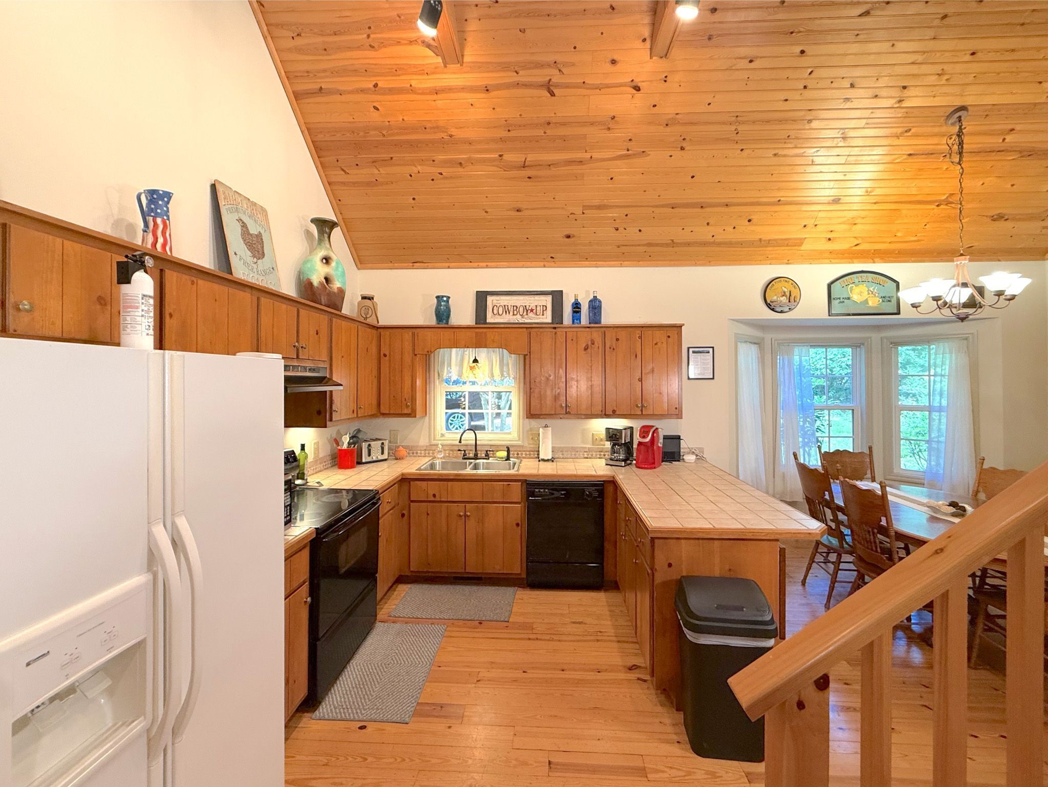 A kitchen with wooden cabinets, a refrigerator, a sink, and a dining area with chairs.