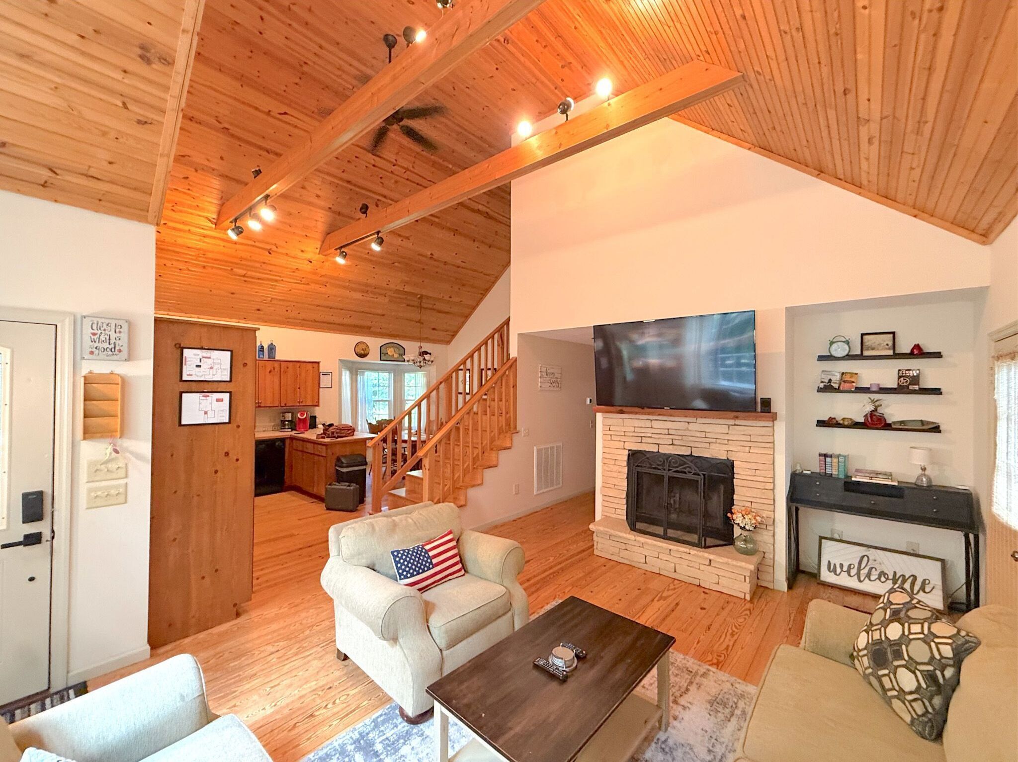 A spacious living room with a fireplace, a television mounted above it, and a staircase leading to the upper floor.