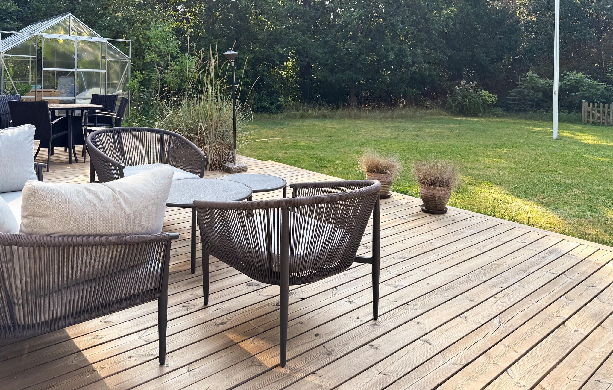 Eine Holzterrasse mit Korbmöbeln und einem Gewächshaus aus Glas.