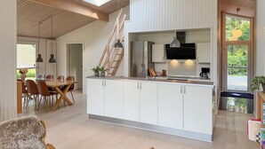 A modern kitchen with white cabinets, a stainless steel refrigerator, and a built-in oven. There is a dining area with a wooden table and chairs, and a large window providing natural light. - Beautiful home in Ebeltoft with WiFi (Ebeltoft)