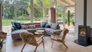 A modern living room with a sectional sofa, two wooden chairs, a round coffee table, and a fireplace. - Beautiful home in Ebeltoft with WiFi (Ebeltoft)