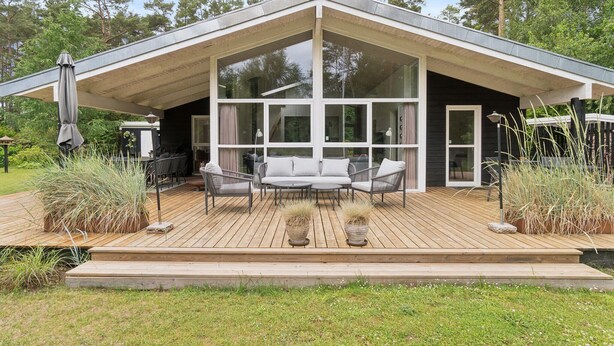 A modern house with a large glass front, a wooden deck, and outdoor furniture. - Beautiful home in Ebeltoft with WiFi (Ebeltoft)