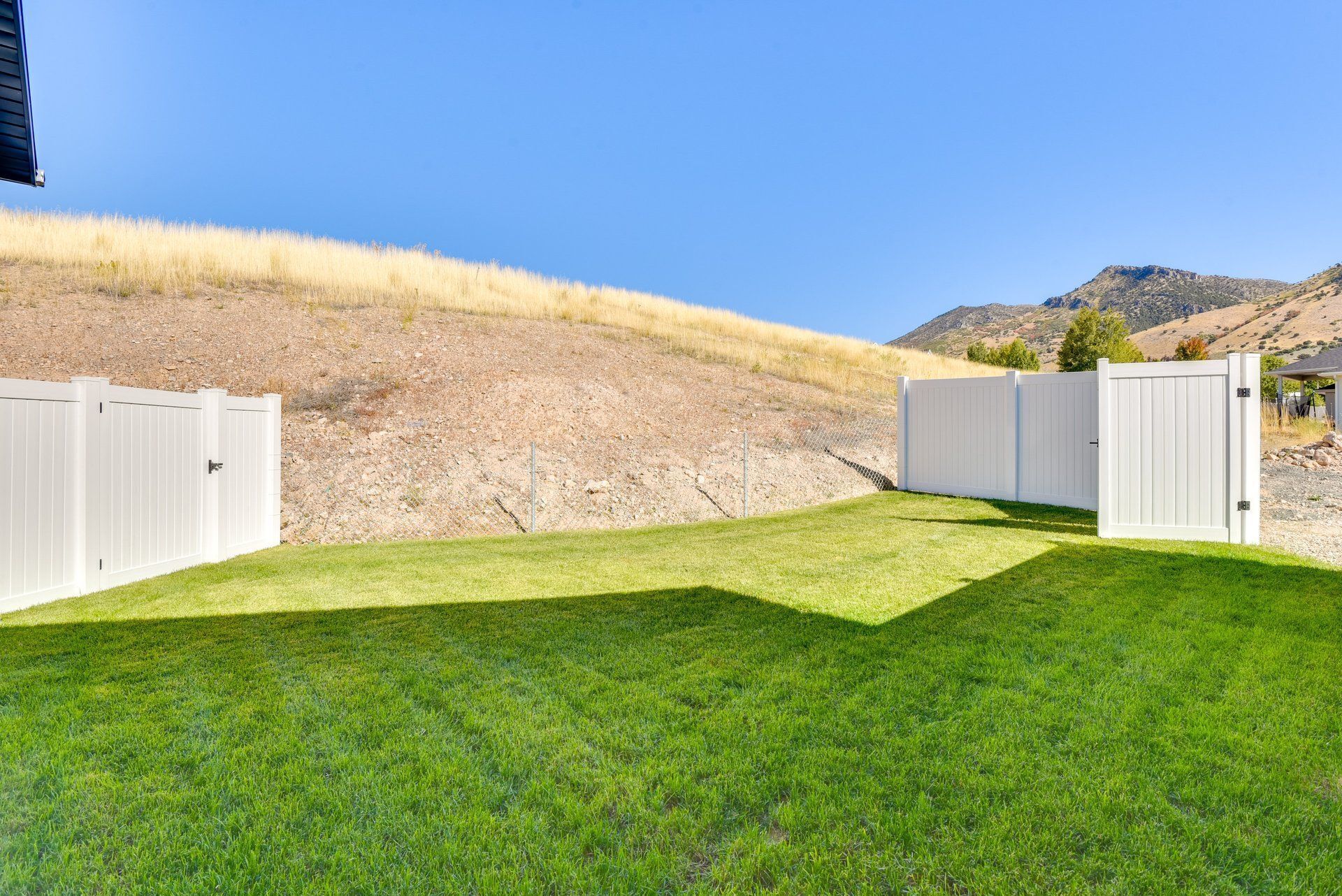 Un patio trasero cercado con césped y un paisaje ondulado al fondo.