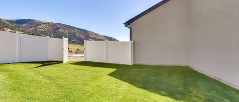Ein gepflegter Garten mit weißem Zaun, einer grünen Rasenfläche und freiem Blick auf ein Gebirge im Hintergrund.