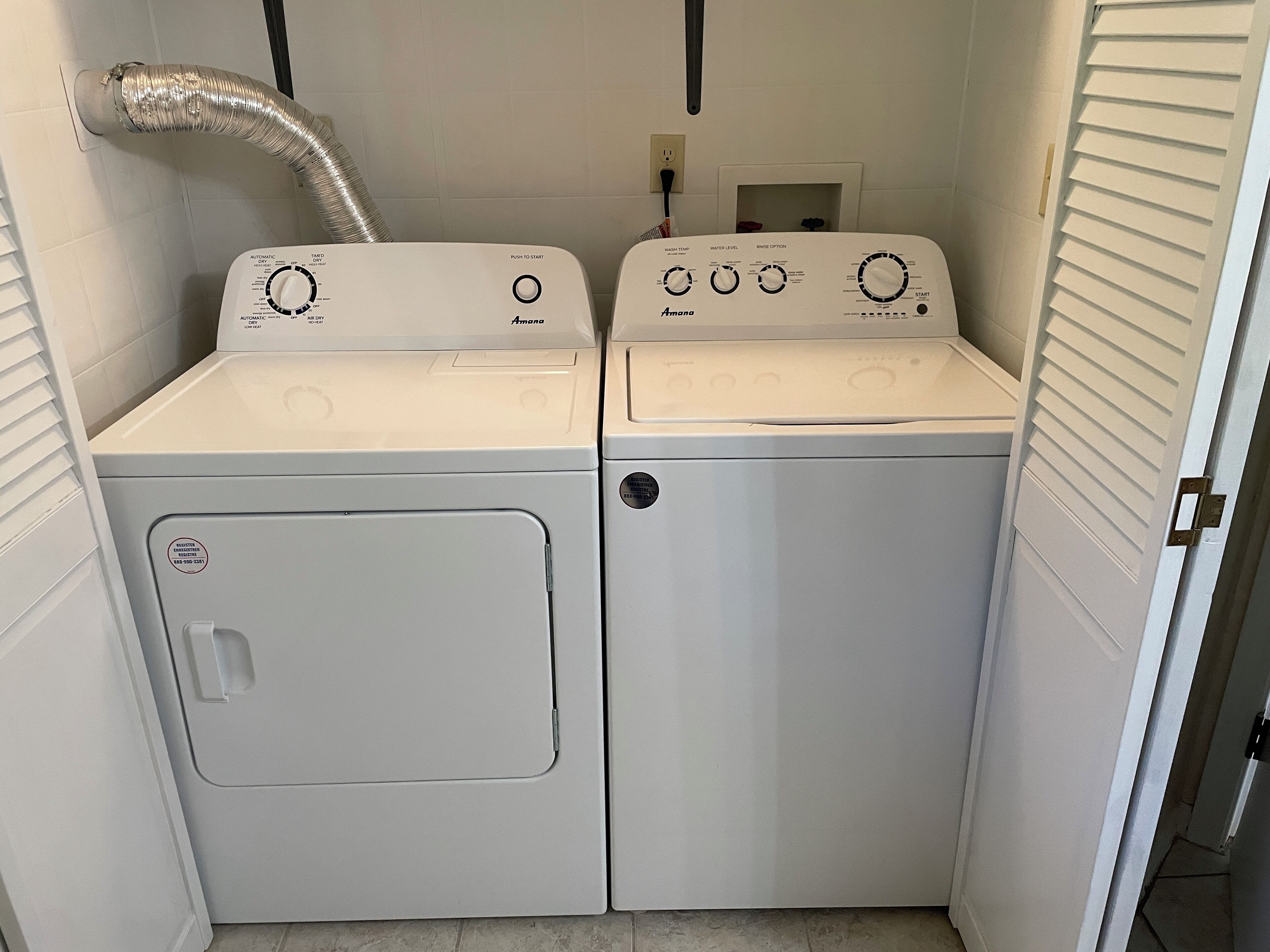 Ett tvättrum med två tvättmaskiner och torktumlare staplade ovanpå varandra, en ventilationsslang och en kontrollpanel med olika inställningar.