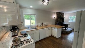 A modern kitchen with white cabinets, a stone fireplace, and a wooden countertop.