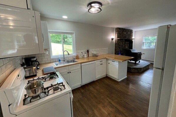 A modern kitchen with white cabinets, a stone fireplace, and a wooden countertop. - Private 5-Acre Farmhouse Retreat - Bethel Woods 25 min - Sleeps 8 - Pets Welcome (Livingston Manor)