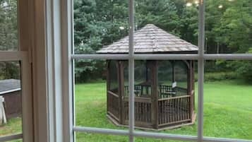 A wooden gazebo with a metal railing, surrounded by a grassy lawn and trees.