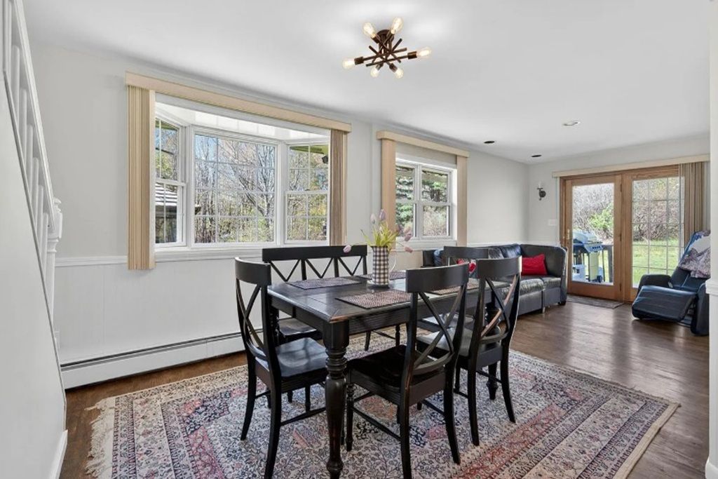 A dining area with a table and chairs, large windows, and a ceiling light fixture.