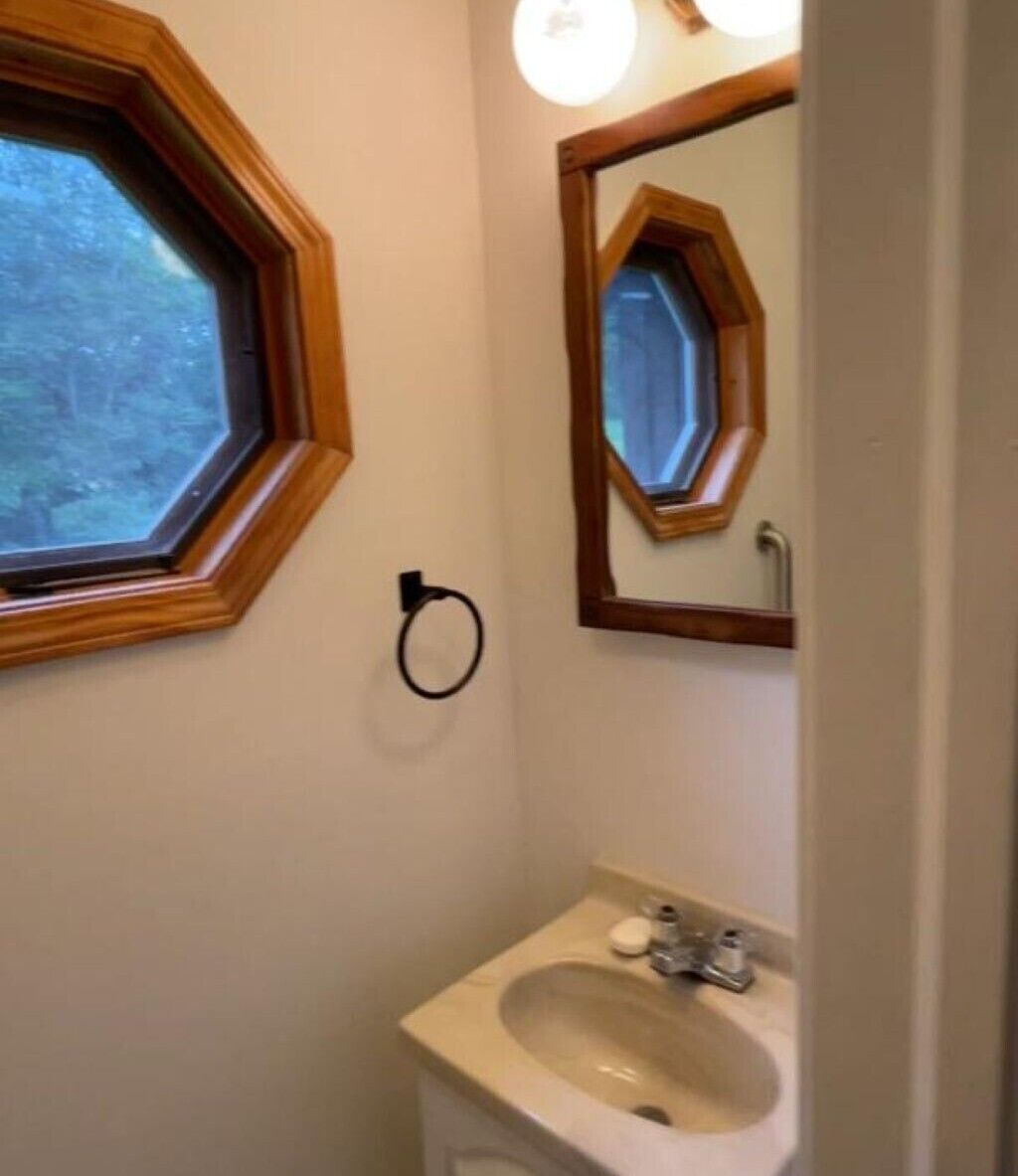 A bathroom with a hexagonal window, a sink, and a mirror with a wooden frame.