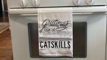 Una cocina con estufa blanca, un reloj digital y una toalla colgada en la puerta del horno con la inscripción 'Greetings from the Catskills'.