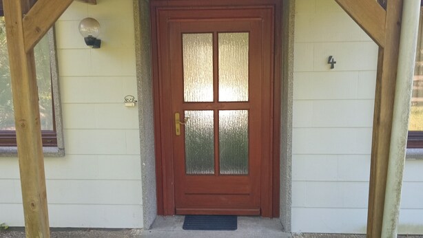 A house with a wooden porch, a brown door with frosted glass panels, and a small doormat.