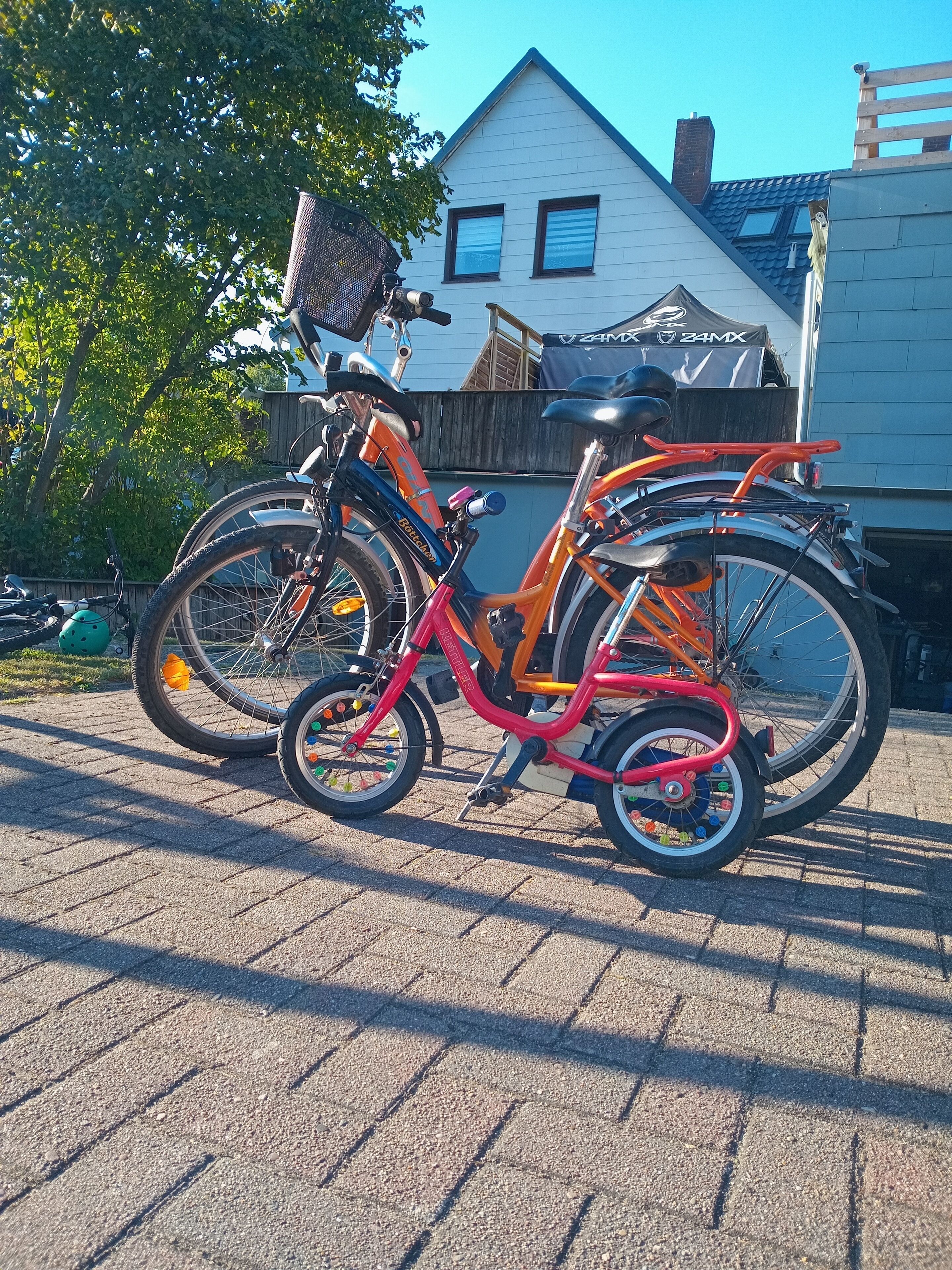 Un vélo rouge et orange est garé sur une surface pavée, avec une maison en arrière-plan.