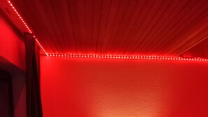 A room with a white dresser, a black monitor, and a red ambient light strip.