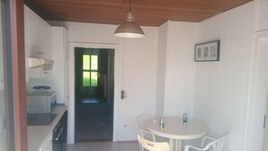A kitchen with a stove, sink, and a window. There is a dining table with chairs and a ceiling light.