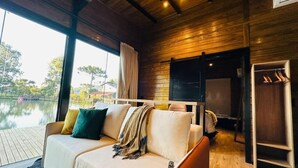 Une pièce chaleureuse avec un plafond en bois, un canapé agrémenté de coussins, un plancher en bois et une vue sur une étendue d’eau à l’extérieur.
