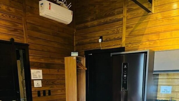 Interior acogedor de una cabaña con un sofá, una pared de madera, un refrigerador negro y una pequeña cocina.