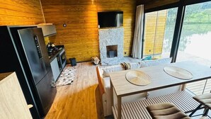 Une cuisine moderne dotée d’une cheminée en pierre, d’un plafond en bois et de grandes fenêtres donnant sur un paysage naturel.