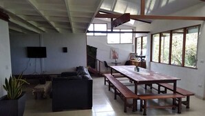 Un salón amplio con una gran mesa de madera y bancos, un sofá y un televisor fijado a la pared.