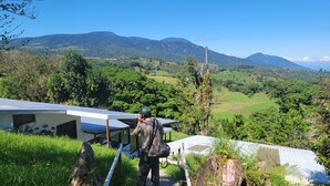 Una persona de pie sobre una cubierta de madera con paneles solares, contemplando un paisaje verde y exuberante con colinas y un cielo despejado.