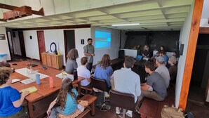 Un aula con una pantalla de presentación, escritorios de madera y sillas dispuestas para una sesión grupal.