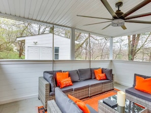 A covered porch with a ceiling fan, a gray sofa with orange cushions, and a view of a white garage.