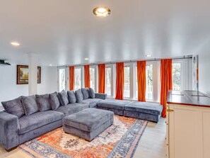 Un salon moderne avec un canapé d’angle, un petit pouf et un tapis à motifs.
