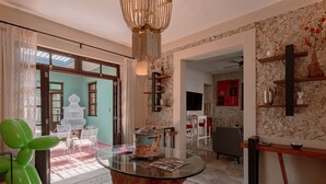 A spacious living area with a glass coffee table, a chandelier, and a stone wall. - Casa Perro Verde very close to Paseo de Montejo (Mérida)