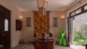 A room with a round glass table, a chandelier, patterned wall decor, and a view of a garden through a glass door. - Casa Perro Verde very close to Paseo de Montejo (Mérida)