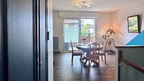Un coin repas avec une table ronde et des chaises, une plante en pot, et une vue sur l’extérieur à travers une porte vitrée.