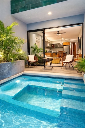 A swimming pool with a glass enclosure, surrounded by lounge chairs and potted plants.