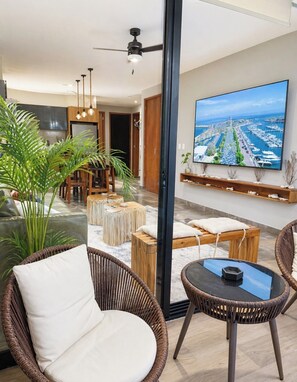 Una sala de estar moderna con un televisor grande, muebles de mimbre y vistas a un puerto deportivo.