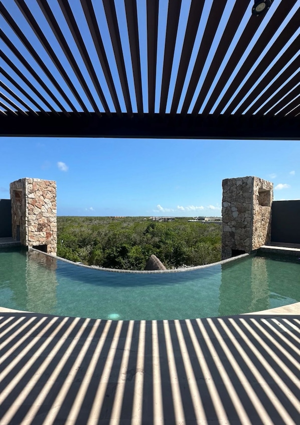 A rooftop infinity pool with stone pillars, a clear blue sky, and a distant view of a landscape.