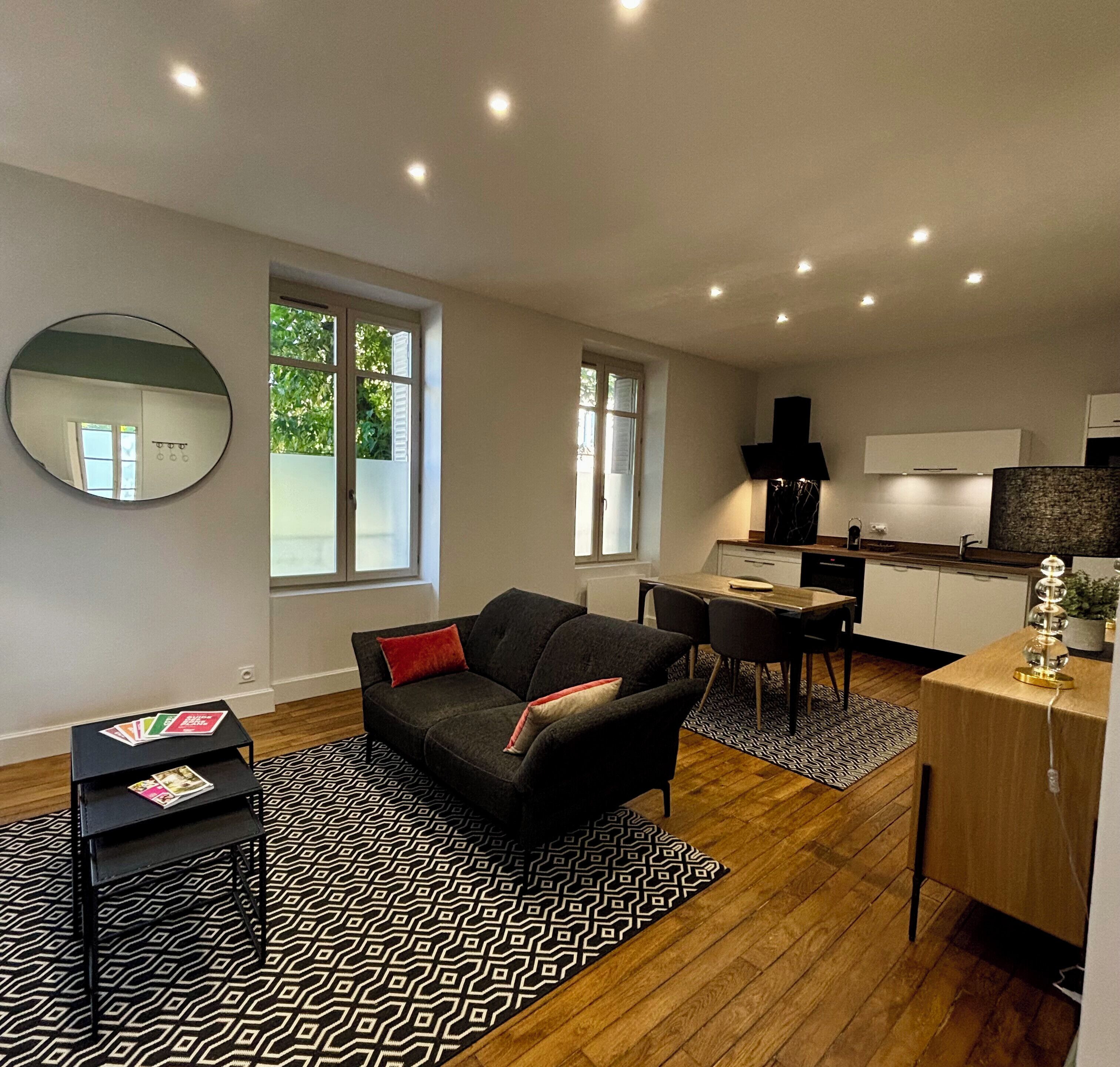 A modern living room with a black sofa, a dining table, and a kitchen area with white cabinets and a black countertop.