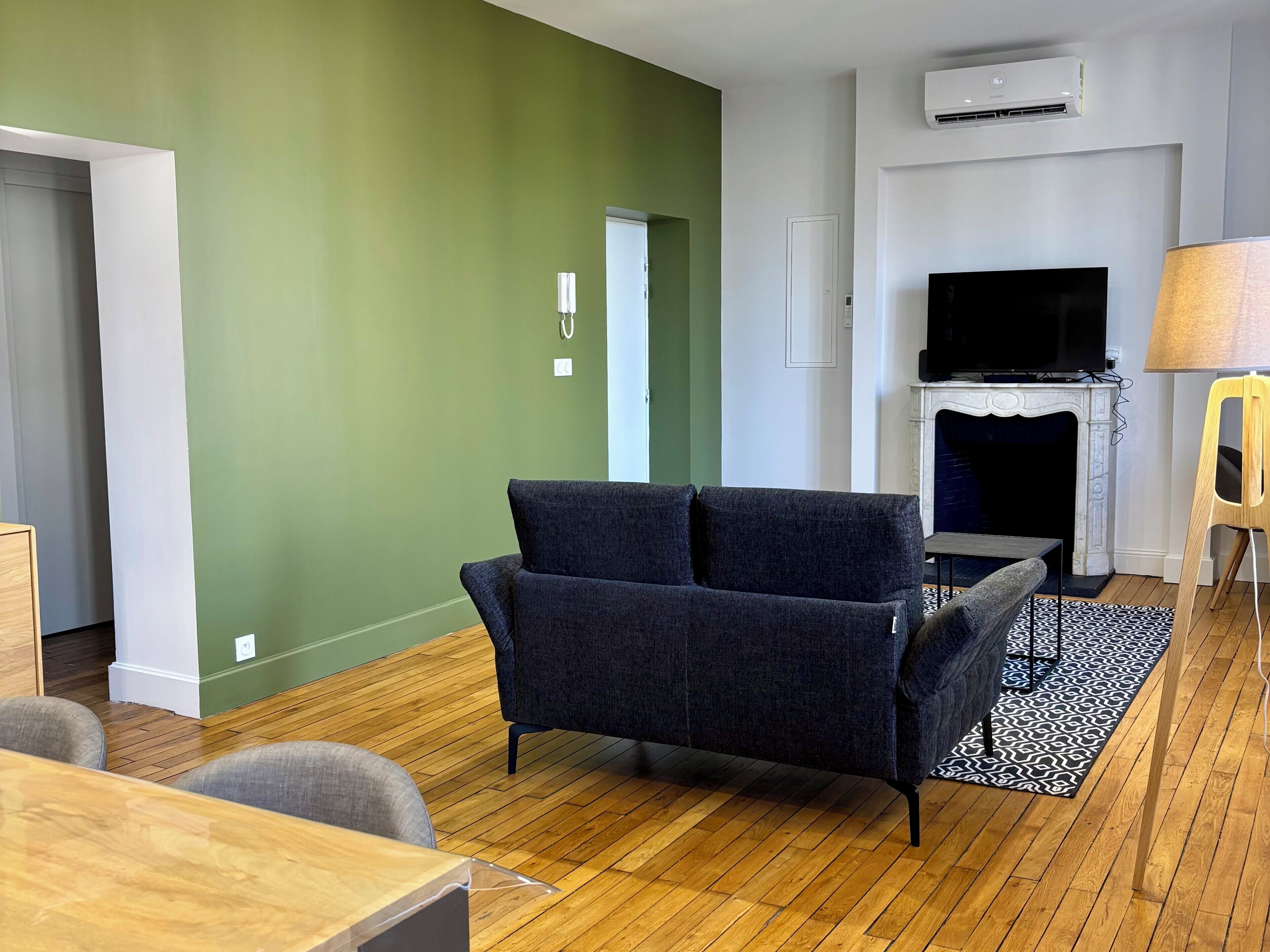 Een woonkamer met een donkere bank, een open haard, een televisie en een houten vloer.
