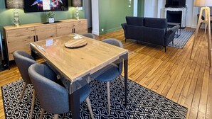 A modern living room with a wooden dining table, grey sofas, and a fireplace.