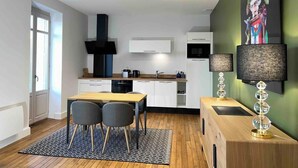 A modern kitchen with white cabinets, a black range hood, and a dining area with a wooden table and two chairs.