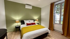 A bedroom with a bed, bedside lamps, a window with curtains, and an air conditioning unit.