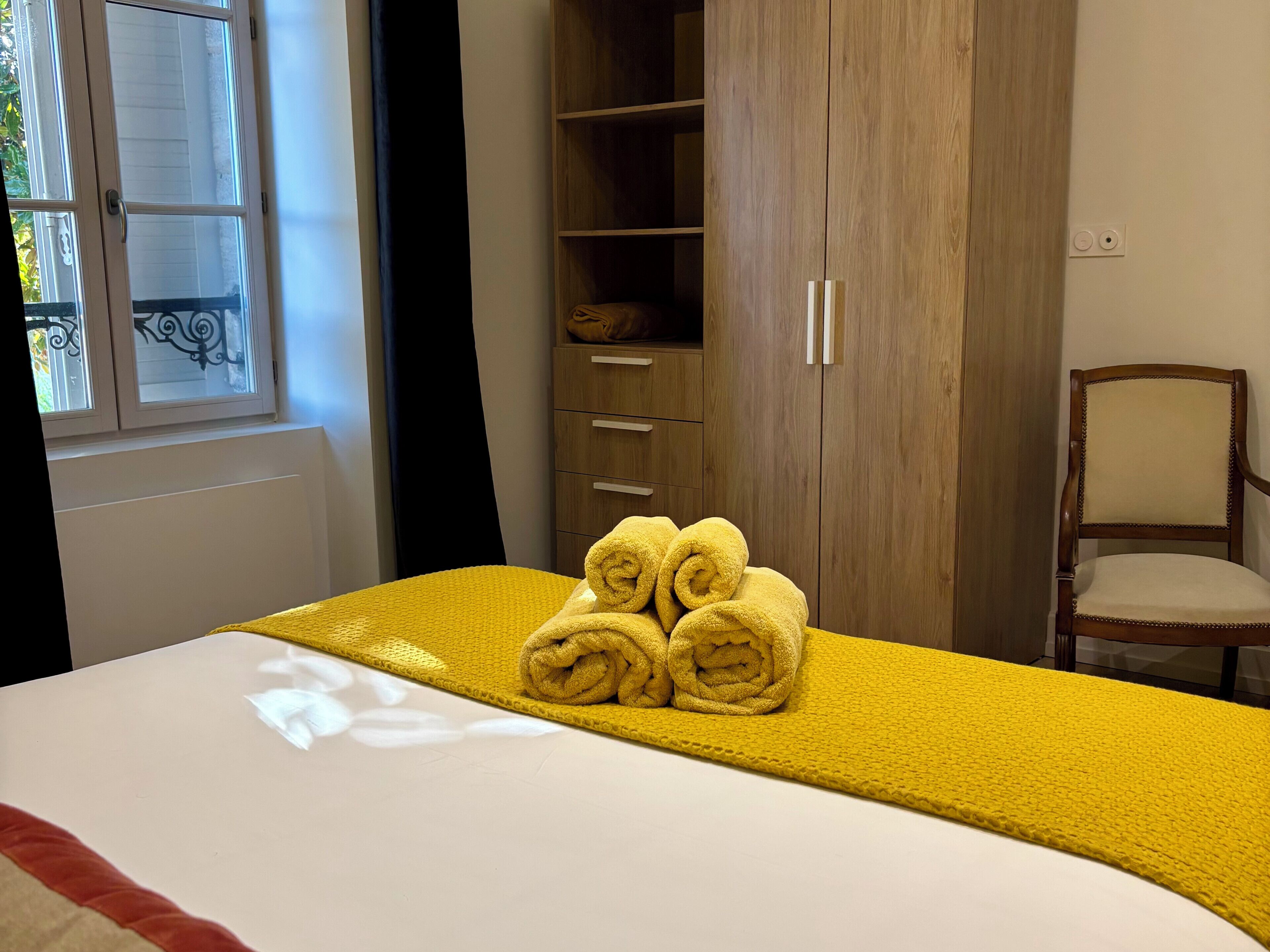 A hotel room with a bed, a wooden wardrobe, and a chair.