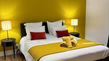 A neatly made bed with white linens, a yellow throw blanket, and a rolled towel. There are two bedside lamps with white shades, and the walls are painted yellow.