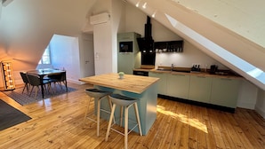 A modern loft apartment with a dining area, kitchen, and a sloped ceiling.