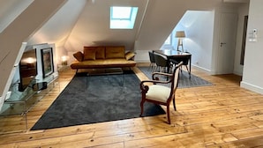 A loft-style room with a sloped ceiling, a sofa, a chair, a table, and a fireplace.