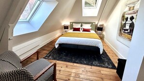 A bedroom with a skylight, a bed with white and red bedding, a black rug, and a wooden floor.