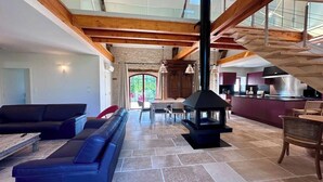 A spacious living area with a stone floor, a black fireplace, and a modern kitchen in the background.