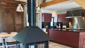 A modern kitchen with a central wood-burning stove, stone flooring, and exposed wooden beams.