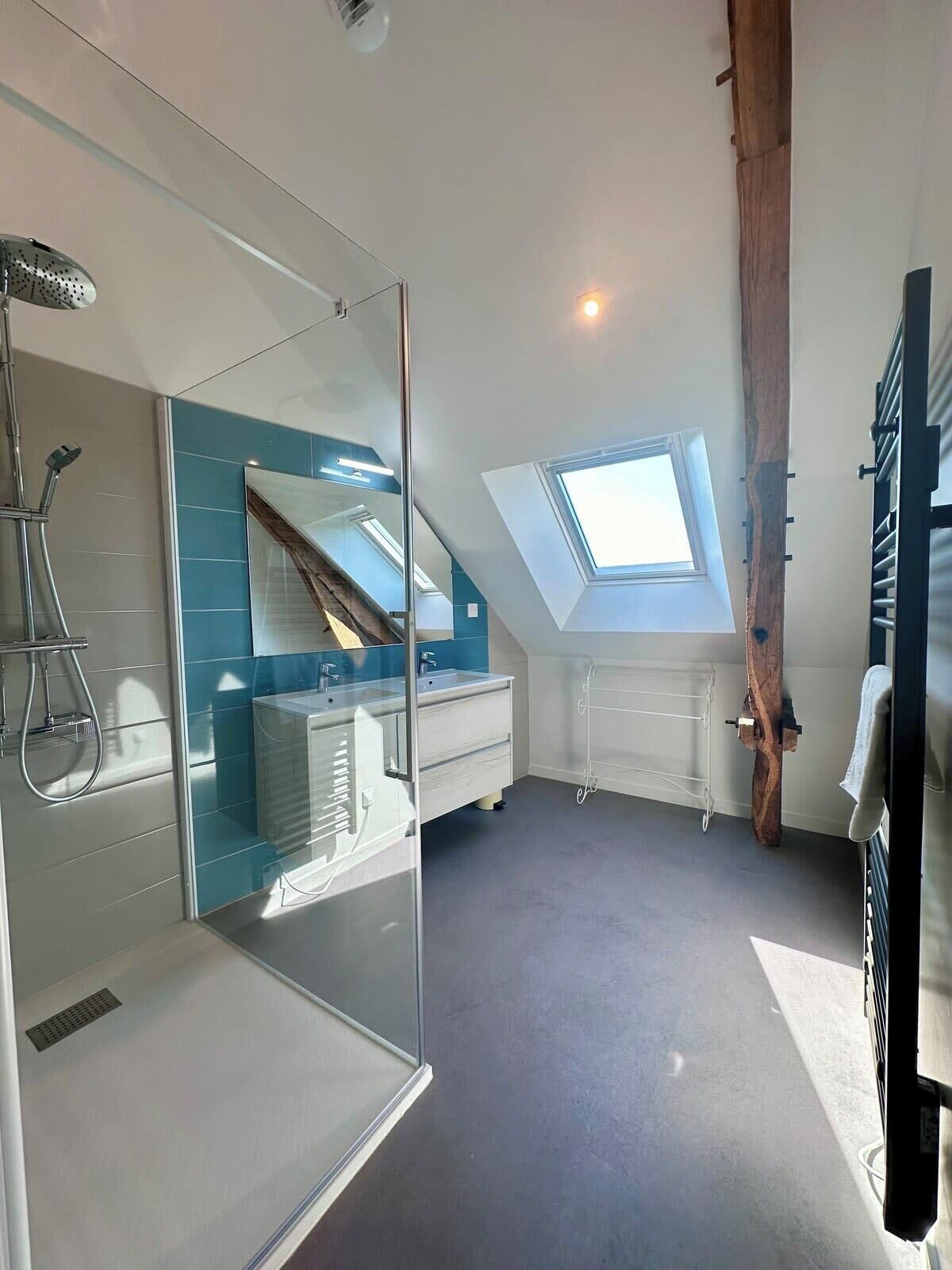 Une salle de bain moderne avec une douche à l’italienne en verre, une lucarne et une poutre en bois.