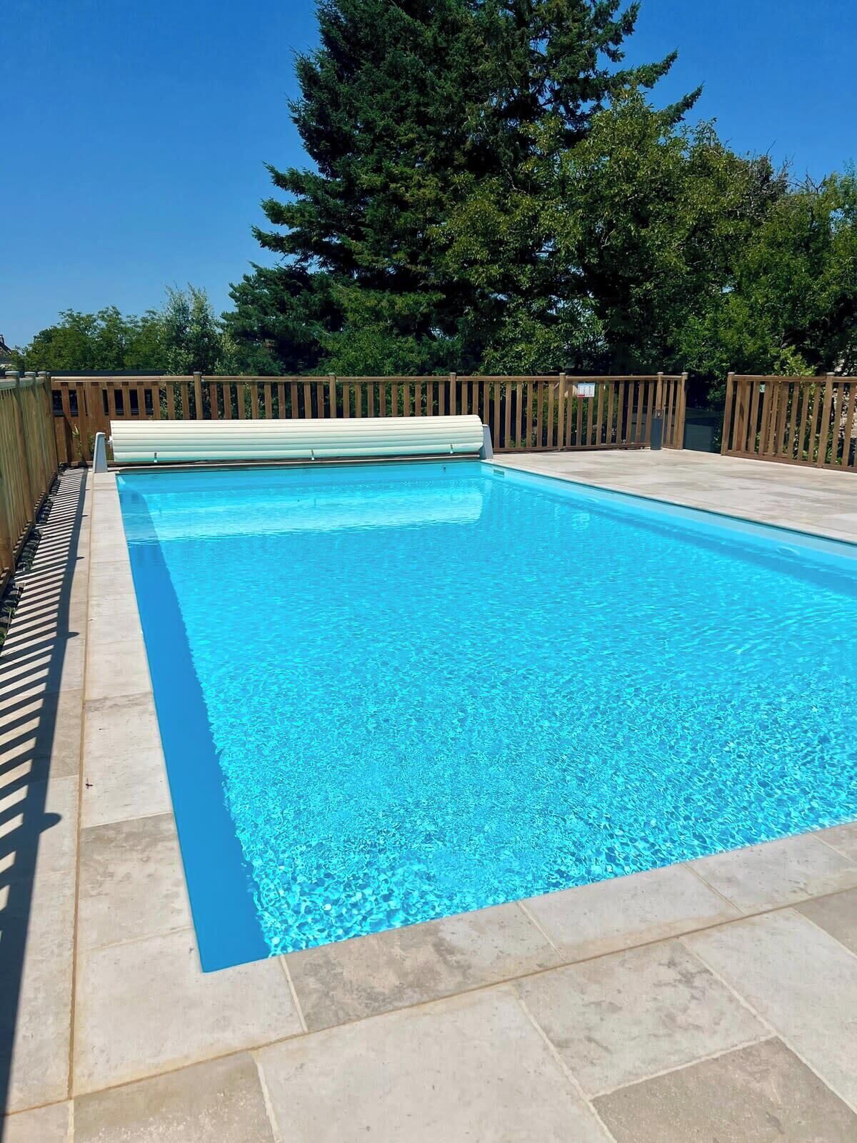 Ein rechteckiger Swimmingpool mit klarem, blauem Wasser, umgeben von einer Holzterrasse und einem Holenzaun.