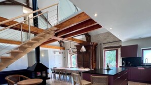 A spacious kitchen with a central island, wooden chairs, and a staircase with exposed beams.