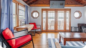 Una habitación con techo de madera, una mesa de comedor, sillas rojas, un sofá y vistas a través de amplios ventanales.