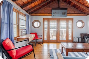 Una stanza con soffitto in legno, un tavolo da pranzo, sedie rosse, un divano e vista attraverso ampie vetrate.